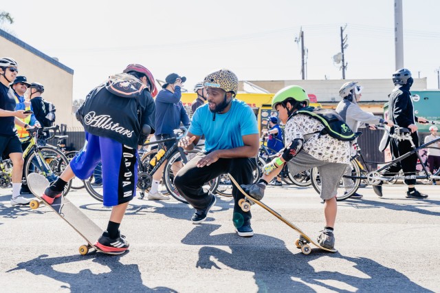 Man kneeling down, giving skateboarding lessons to two young boys